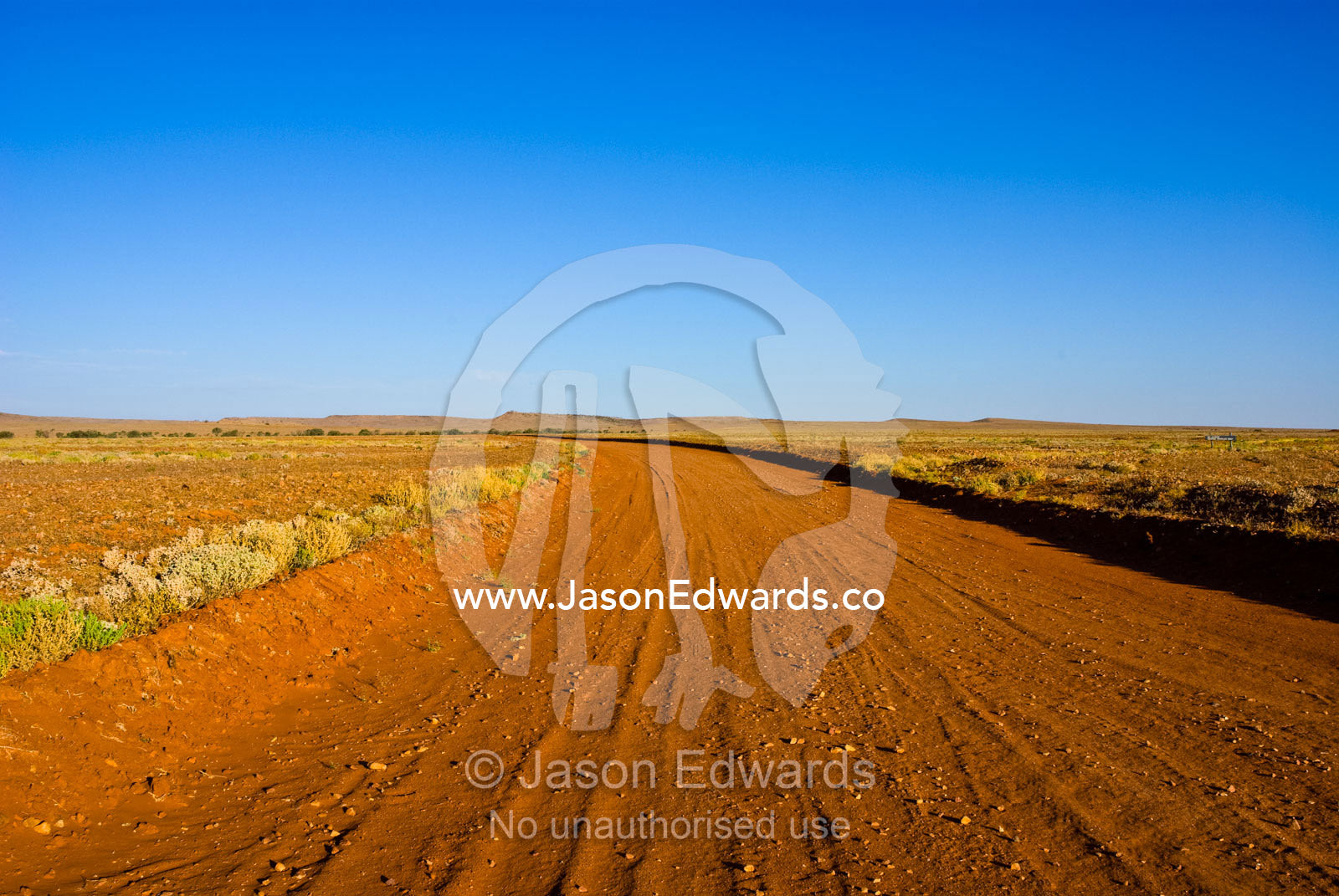 A red sandy track winds over a rugged plain in a remote outback desert Sturt National Park, New South Wales, Australia.