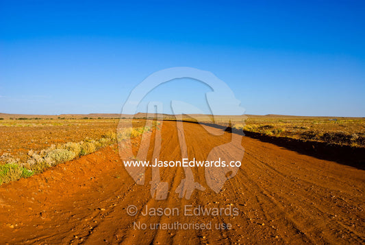 A red sandy track winds over a rugged plain in a remote outback desert Sturt National Park, New South Wales, Australia.