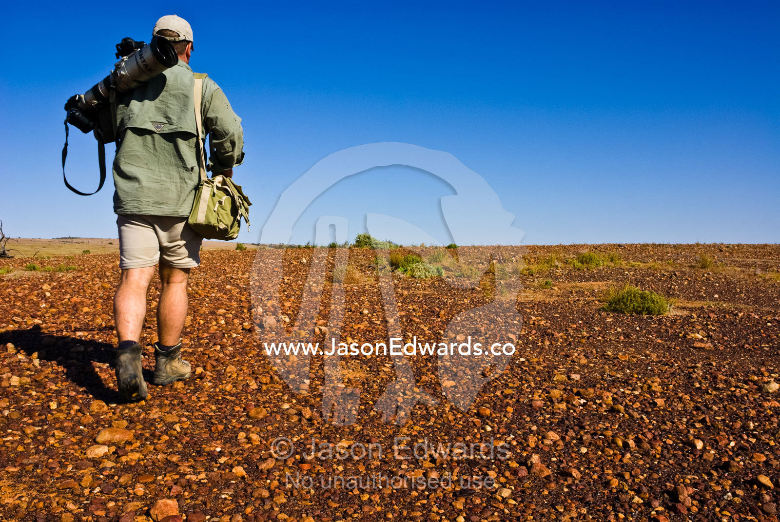 A wildlife photographer carries his camera gear across a remote desert Sturt National Park, New South Wales, Australia.