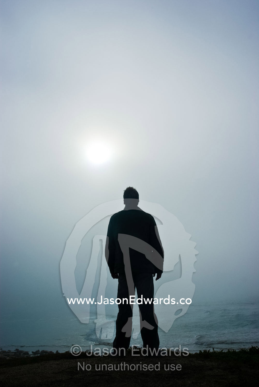 A solitary figure contemplates the heavens as the sun pierces dawn fog Point Impossible, Victoria, Australia.