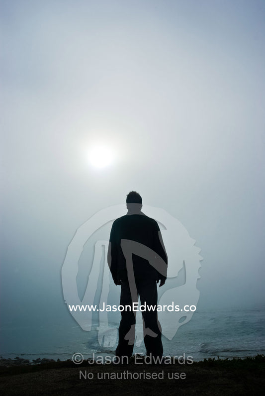 A solitary figure contemplates the heavens as the sun pierces dawn fog Point Impossible, Victoria, Australia.