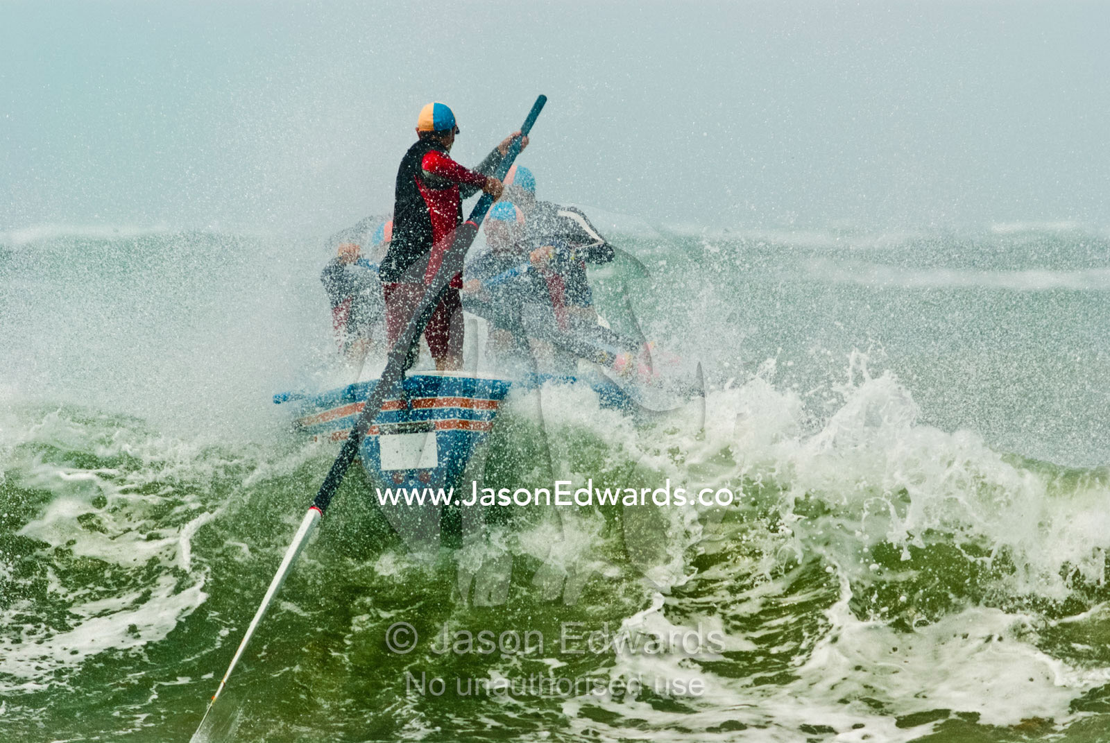 A surf boat crests the top of a green wave in rough seas in a race. Australian Surfboat Open Titles, Fishermen's Bay, Torquay, Victoria, Australia.