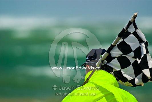 A steward prepares to wave a chequered flag to start a surf boat race. Australian Surfboat Open Titles, Fishermen's Bay, Torquay, Victoria, Australia.