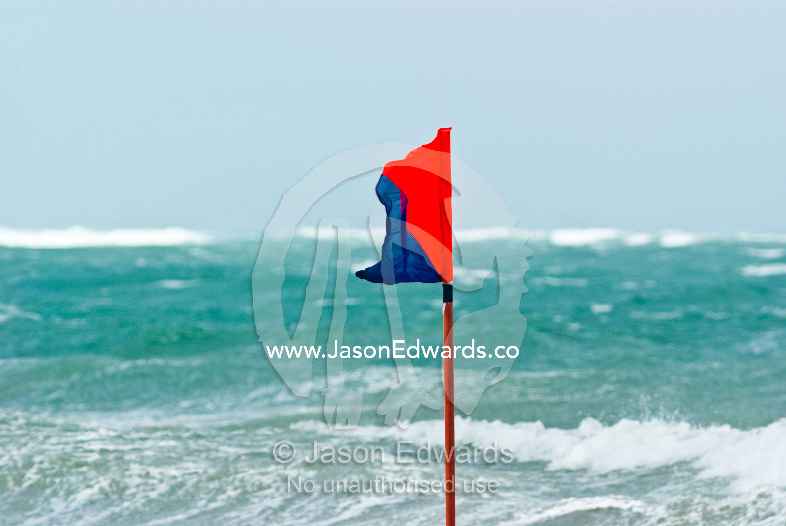 A surf life saving safety flag flaps in gale force winds on a beach. Australian Surfboat Open Titles, Fishermen's Bay, Torquay, Victoria, Australia.