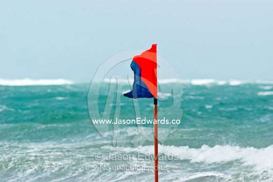 A surf life saving safety flag flaps in gale force winds on a beach. Australian Surfboat Open Titles, Fishermen's Bay, Torquay, Victoria, Australia.
