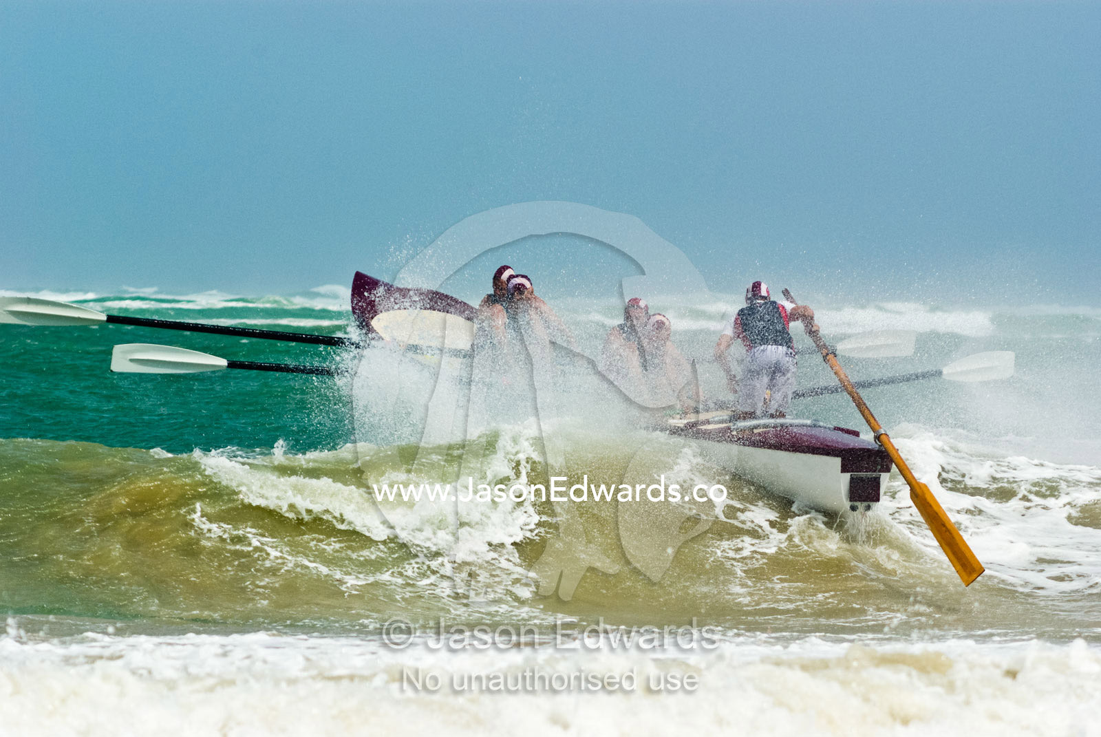 A surf boat crests the top of a green wave in rough seas in a race. Australian Surfboat Open Titles, Fishermen's Bay, Torquay, Victoria, Australia.