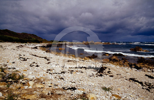 A storm rolls in over a rugged stony beach along the Southern Ocean. South West Conservation Area, Tasmania, Australia.