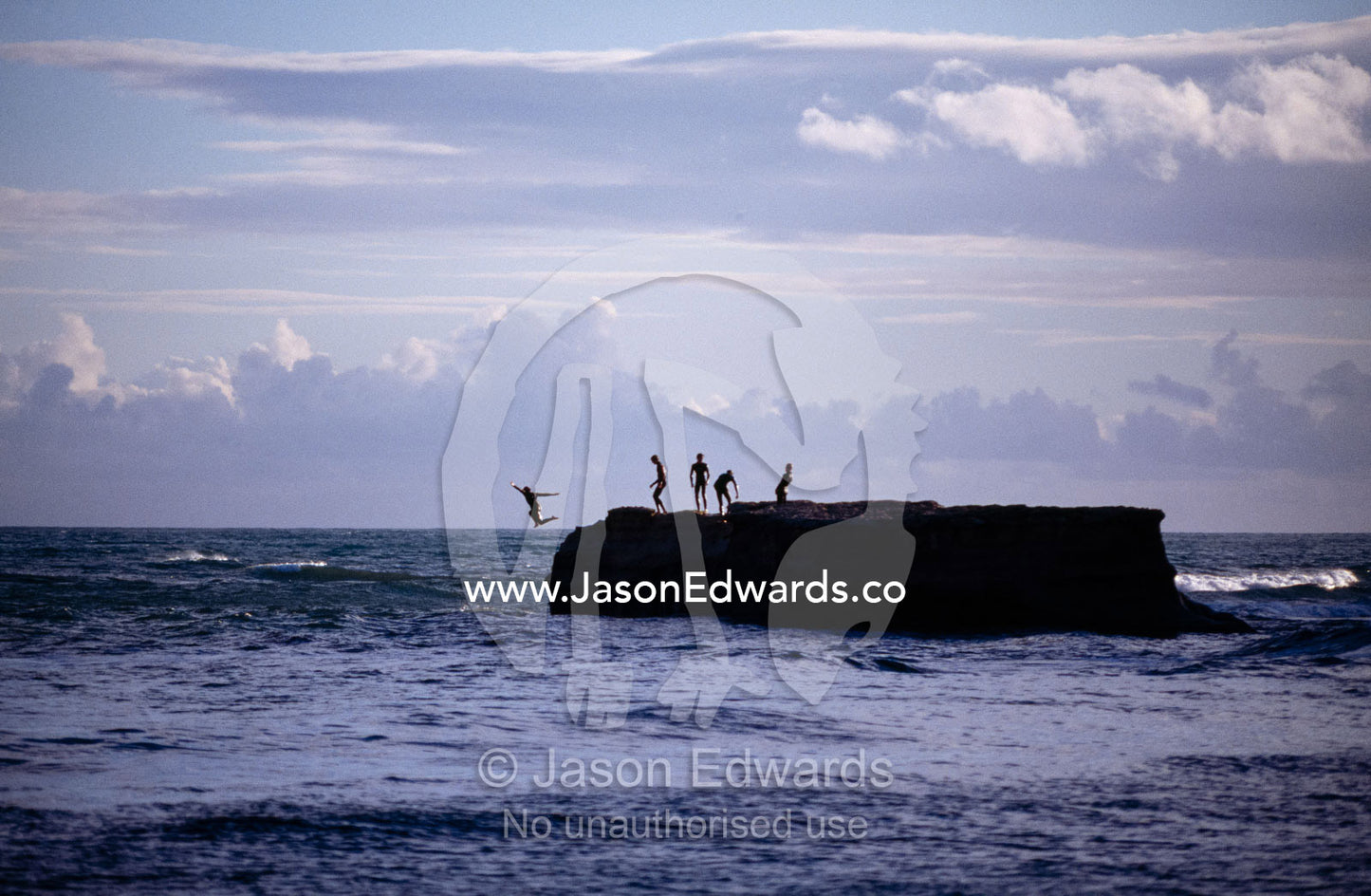 Teenage boys leap from a steep rock rising from the Bass Strait sea. Bird Rock, Jan Juc, Surfcoast, Victoria, Australia.