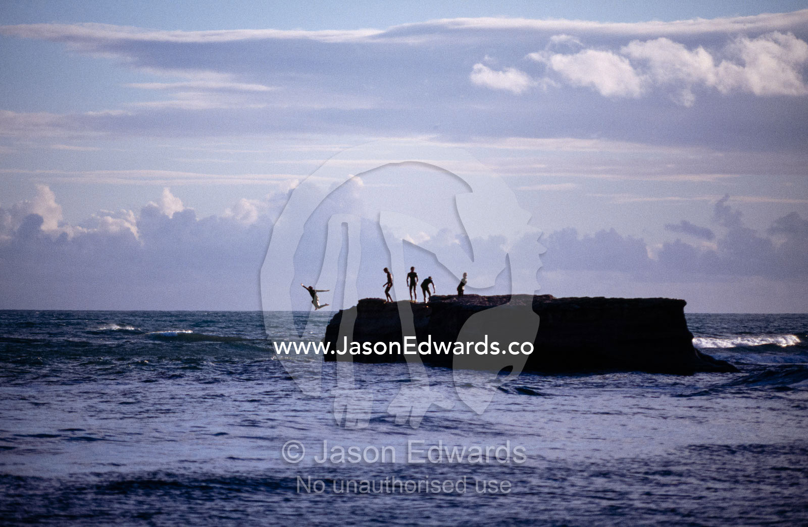Teenage boys leap from a steep rock rising from the Bass Strait sea. Bird Rock, Jan Juc, Surfcoast, Victoria, Australia.