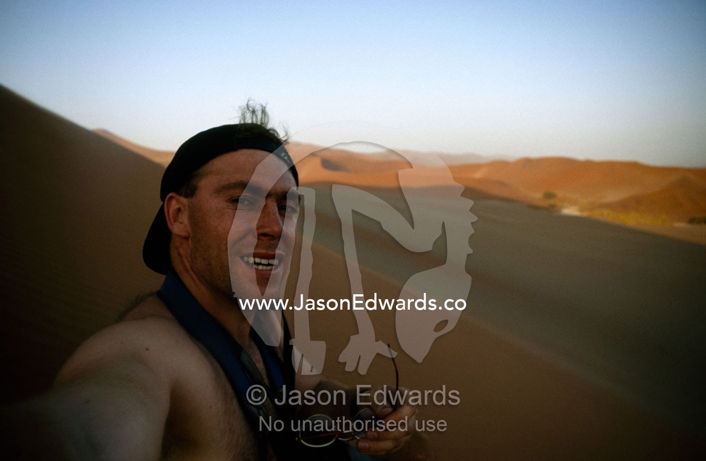 A natural history photographer rests in the shadow of a huge dune. Sossusvlei, Great Southern Dune Field, Namib-Naukluft National Park, Namibia.