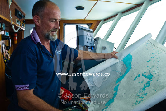 A ships captain examines a maritime map highlighting dangerous reefs. Coral Sea, Coral Sea Islands Territory, Australia.