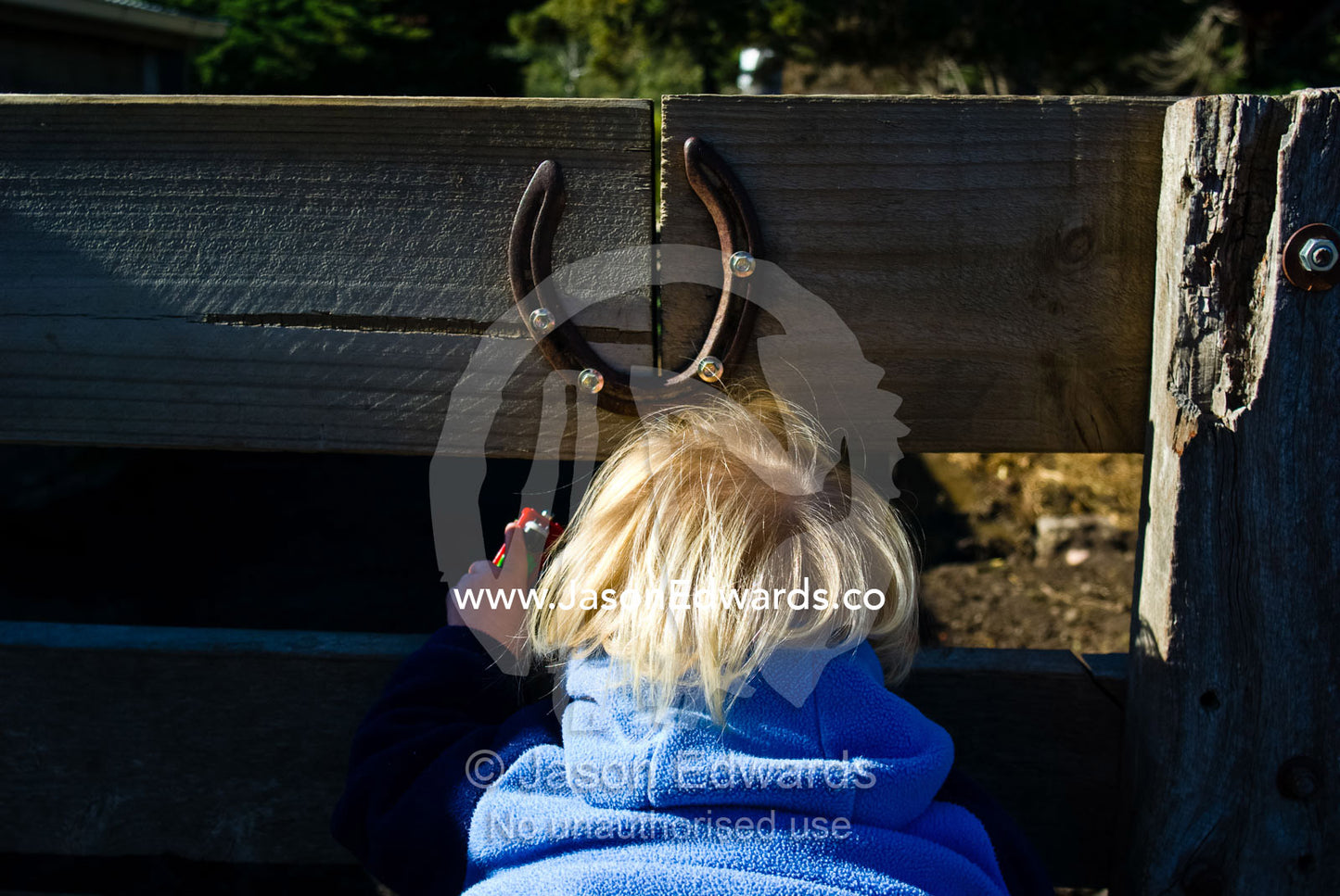 A young boy beneath a lucky horseshoe looks through a farm fence. Collingwood Childrens Farm, Collingwood, Victoria, Australia