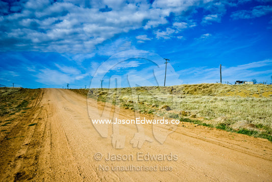 A remote dusty road heads over the horizon to an outback country town. Hughenden, Queensland, Australia