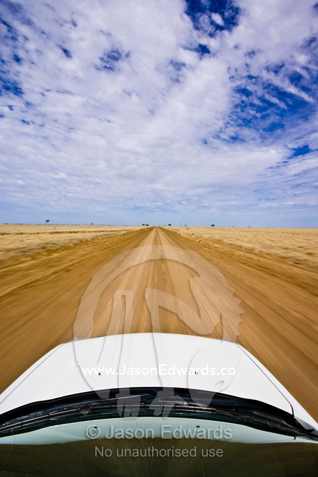 An SUV drives at high speed along a rough dirt road in the Outback. Hughenden Muttaburra Road, Queensland, Australia