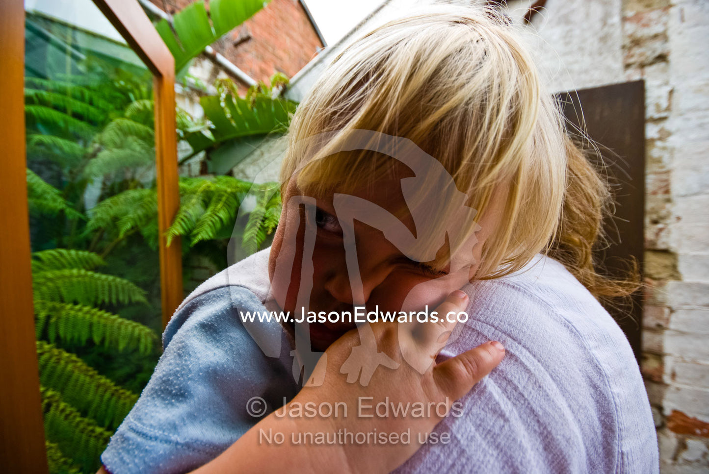 A sad toddler rests his head on his mother's shoulder for a cuddle. Carlton North, Victoria, Australia.