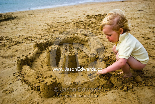 A toddler concentrates while building a sand castle on a beach. Barwon Heads, Bellarine Peninsula, Victoria, Australia.