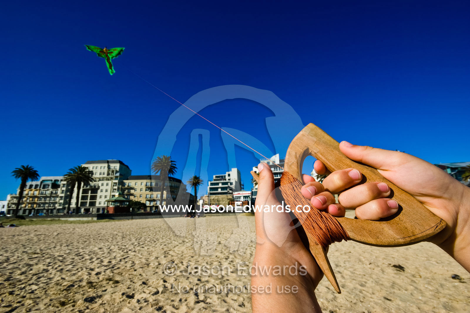 The hands of a young boy flying a bright green Balinese dragon kite. Port Melbourne Beach, Victoria, Australia.