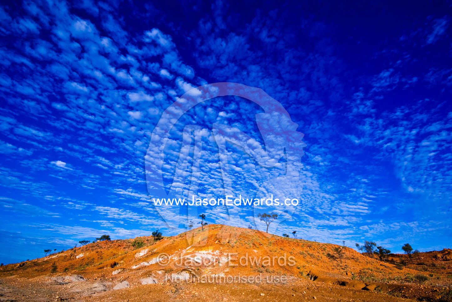 Clouds roll over a volcanic red hill rising from a desert plain. Cramsie Muttaburra Road, Queensland, Australia.