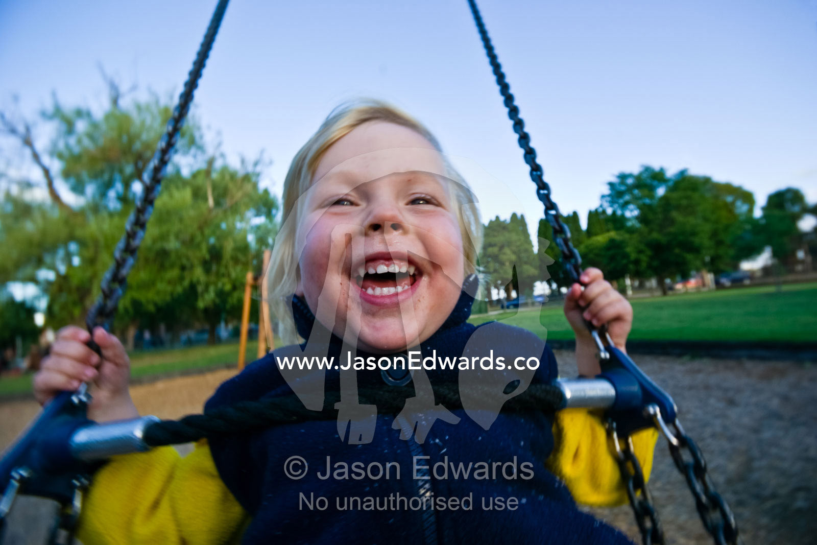 A young boy laughing hysterically as he plays on a swing in a park. Princes Park, Carlton, Victoria, Australia