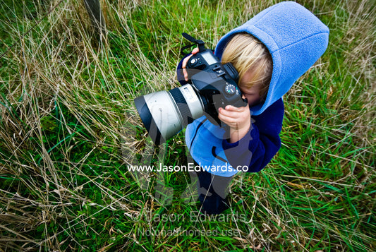 A small boy learning to take photographs in a farm field in winter. near Fish Creek, Victoria, Australia