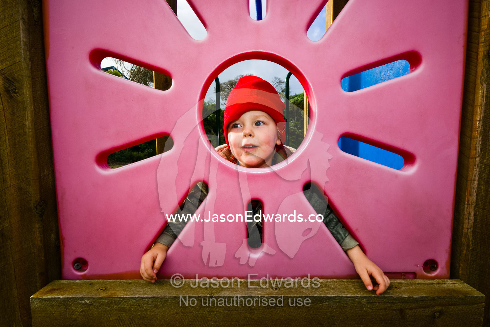 A young boy peers through a sun-shaped window in a playground house. Sandy Point, Victoria, Australia