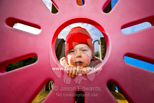 A young boy peers through a sun-shaped window in a playground house. Sandy Point, Victoria, Australia