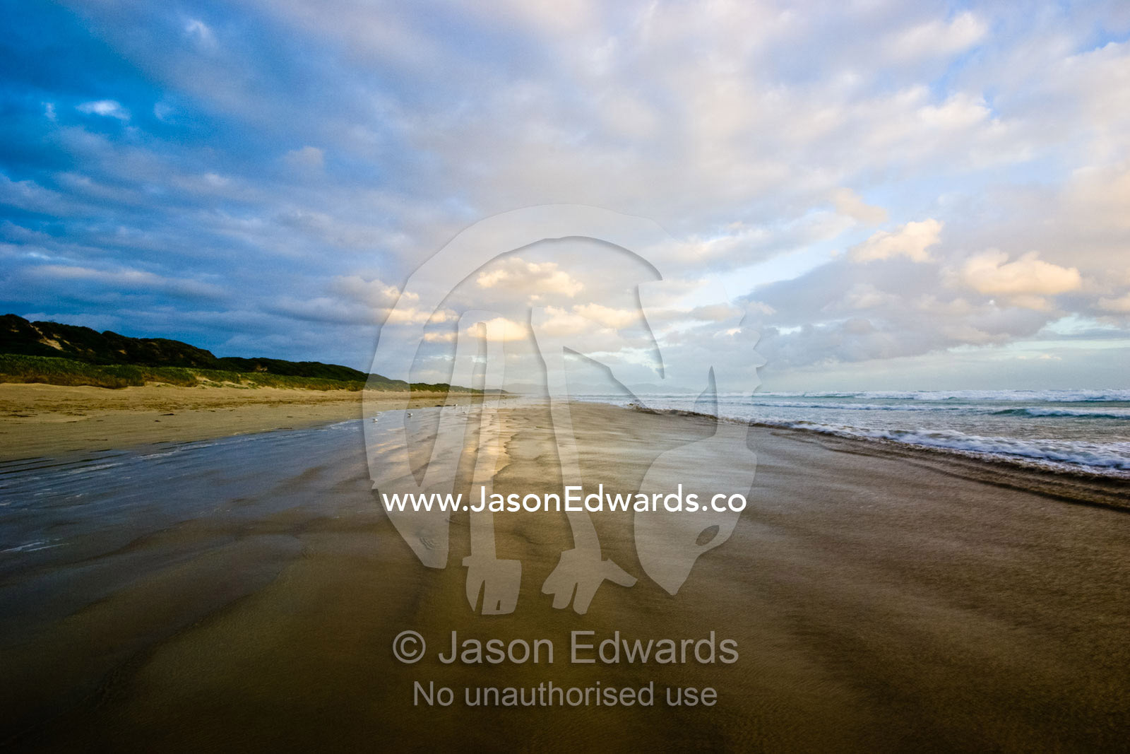 A storm surge wets the sand on a wide empty beach at sunset. Waratah Bay, Victoria, Australia.