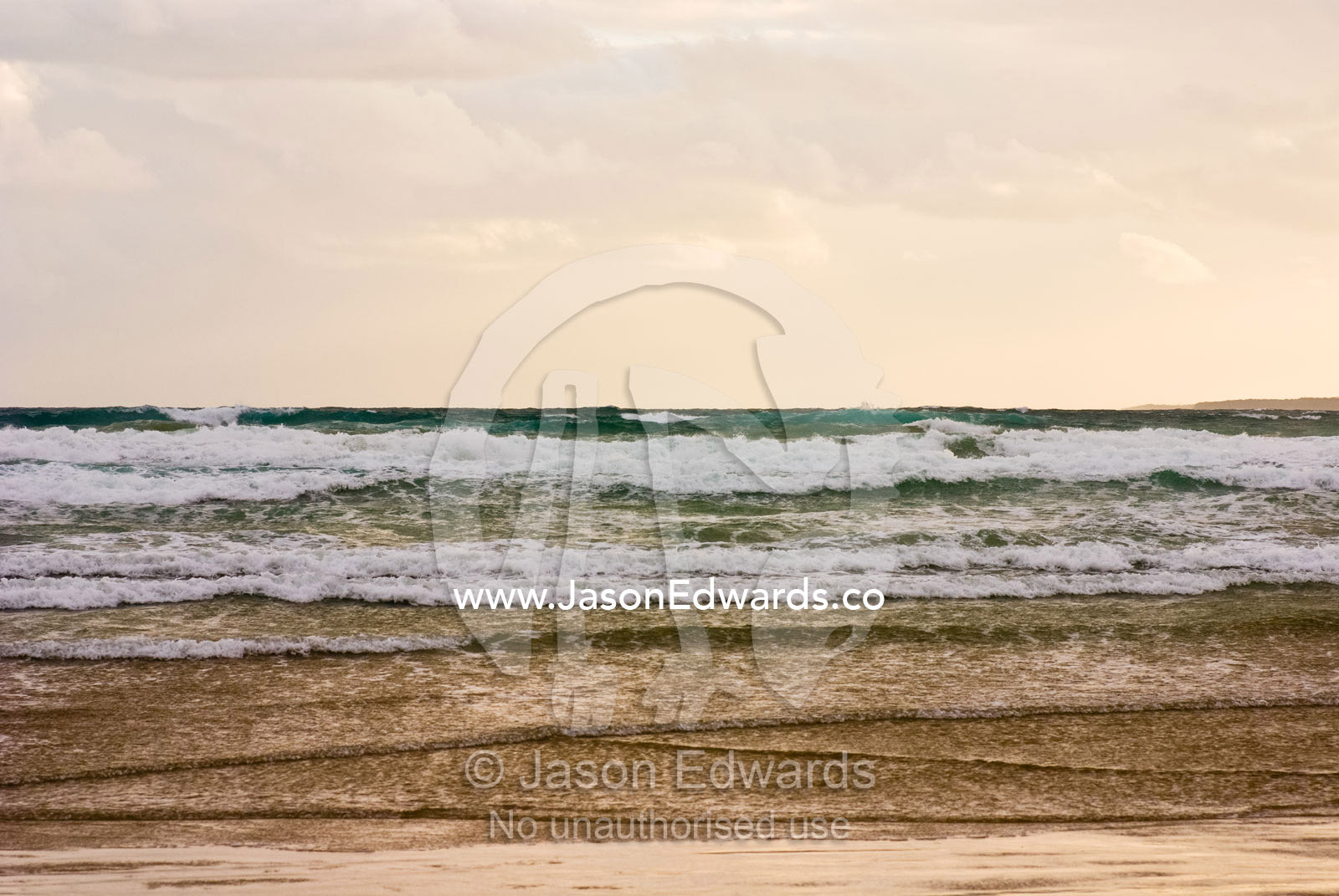 Storm clouds reflect pastel colors in rough waves rolling into shore. Waratah Bay, Victoria, Australia.