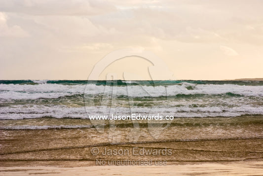 Storm clouds reflect pastel colors in rough waves rolling into shore. Waratah Bay, Victoria, Australia.