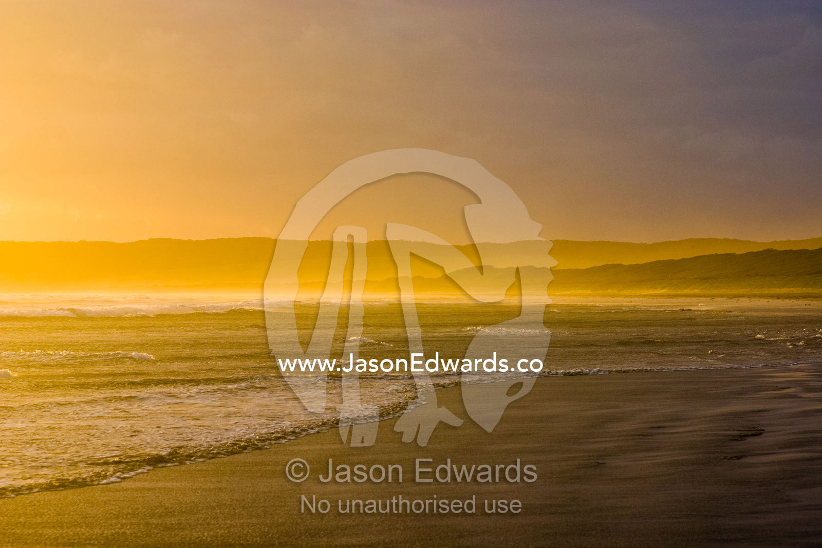 Small waves caress a wide beach in an ocean bay at sunset. Waratah Bay, Victoria, Australia.