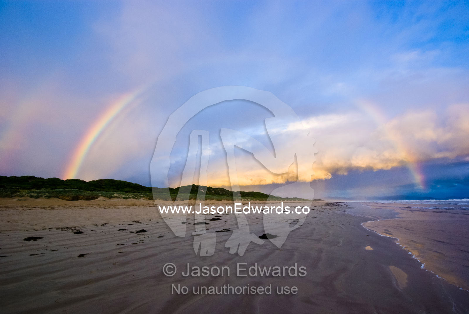 A rainbow crests a storm front over a wide deserted beach at twilight. Waratah Bay, Victoria, Australia.