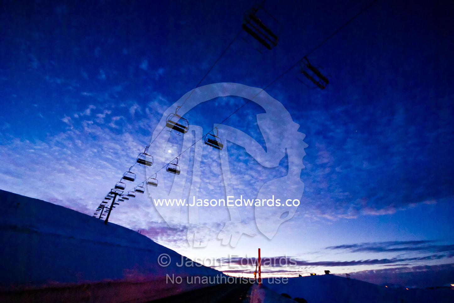 A cable ski chairlift crosses an snowy alpine road after sunset. Mount Hotham, Great Dividing Range, Victoria, Australia