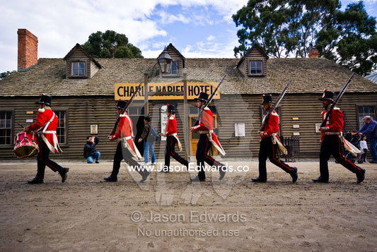A patrol of British Redcoat soldiers march in formation past a hotel. Ballarat, Victoria, Australia.