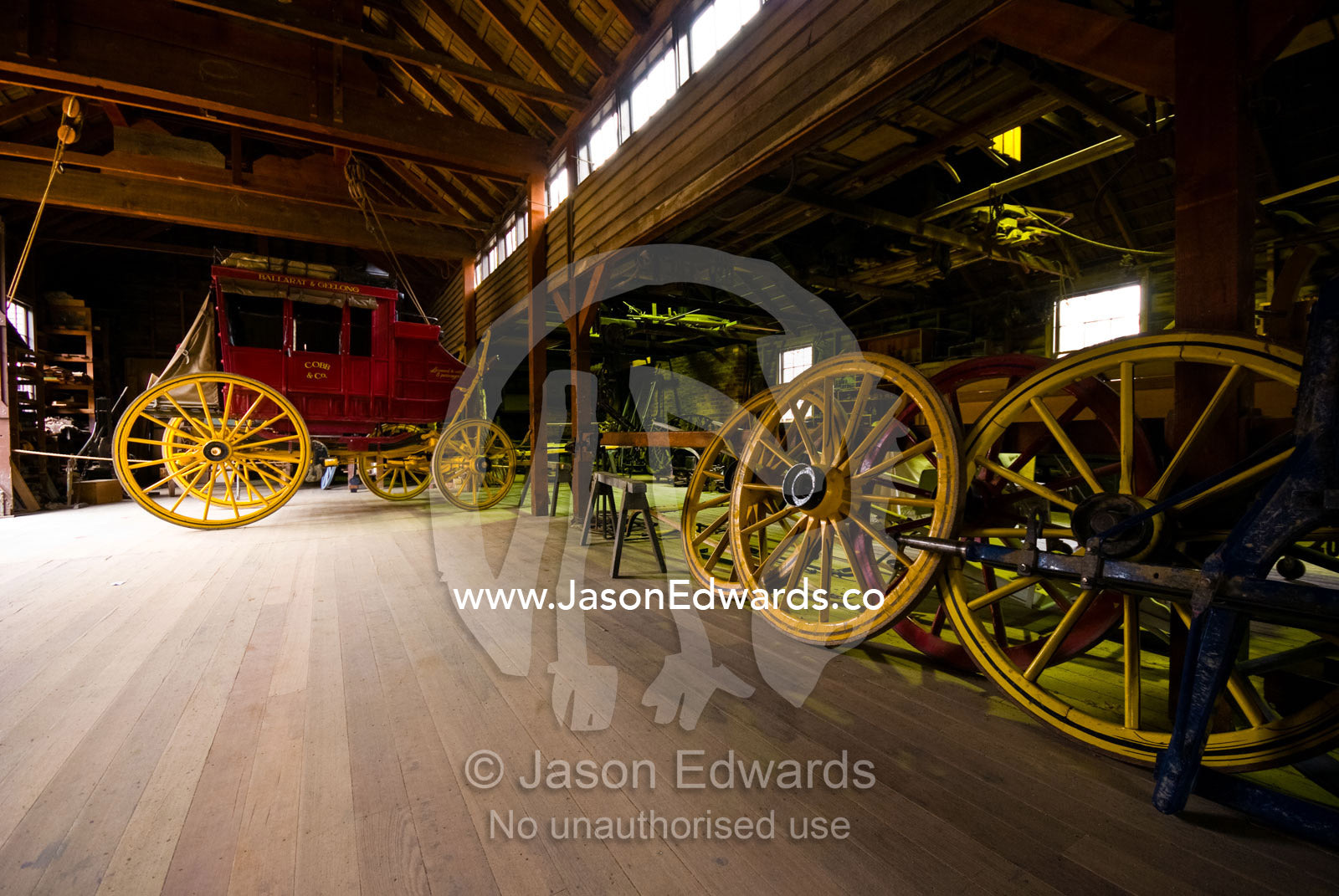 A stagecoach and wagon-wheels await repair in a maintenance workshop. Ballarat, Victoria, Australia.