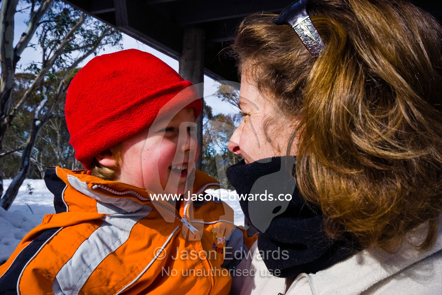 A small boy smiling in his mothers arms on a snowy winter day. Dinner Plain, Great Dividing Range, Victoria, Australia.