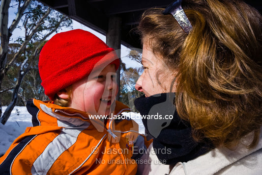 A small boy smiling in his mothers arms on a snowy winter day. Dinner Plain, Great Dividing Range, Victoria, Australia.