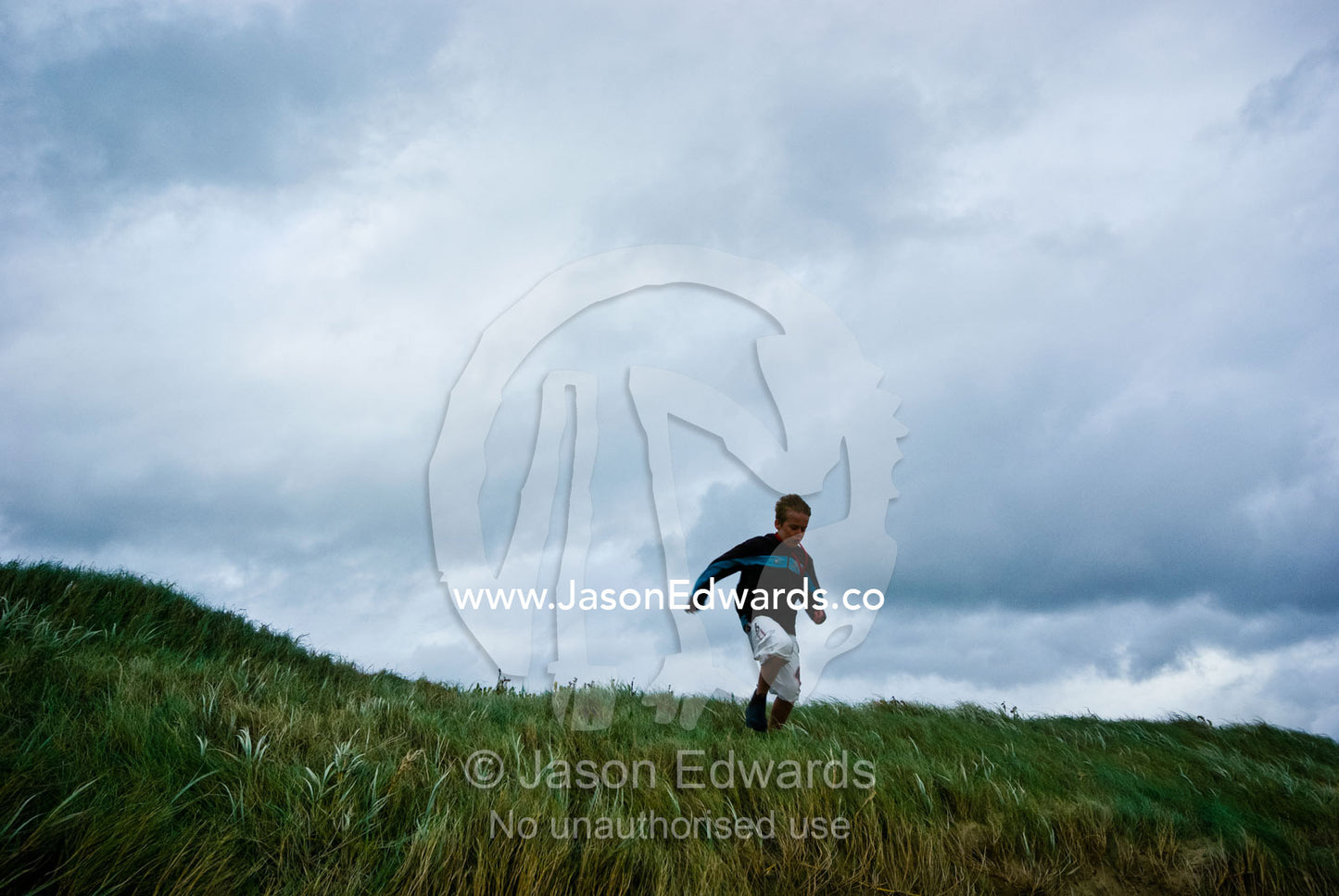 A boy runs though long windblown grass on a stormy winters day. Sandy Point, Victoria, Australia