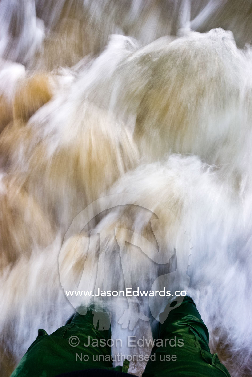 Ocean waves crash in against a mans legs standing in the shallow water Sandy Point, Victoria, Australia