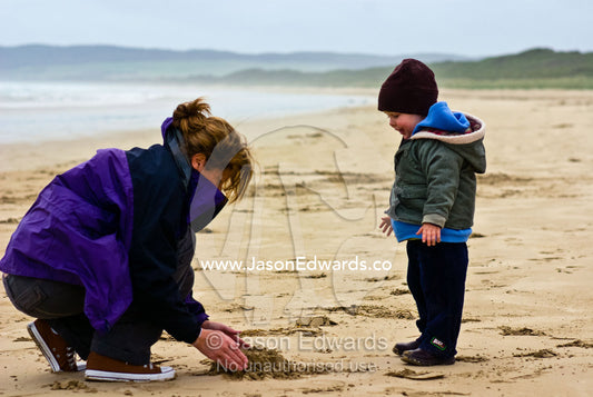 A mother and son build a sand castle on a stormy beach in winter. Sandy Point, Victoria, Australia