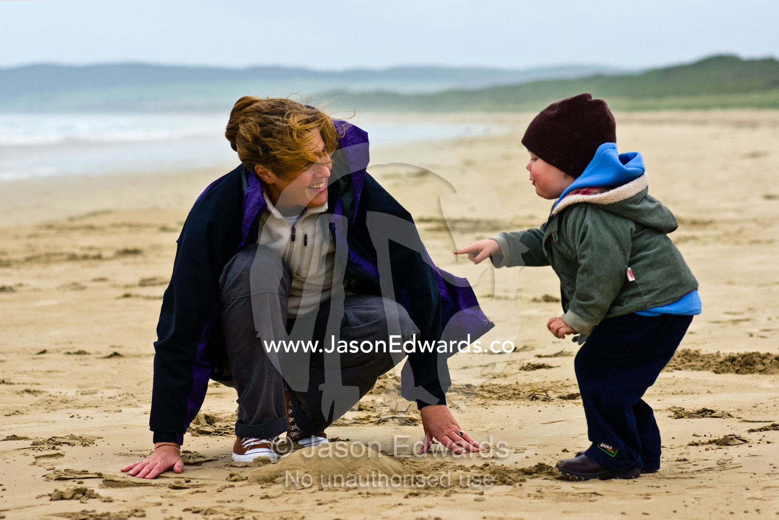 A mother and son build a sand castle on a stormy beach in winter. Sandy Point, Victoria, Australia