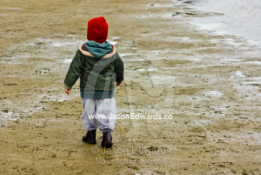 A small boy dressed in winter clothes walking along a river shore. Tidal River, Wilsons Promontory National Park, Victoria, Australia