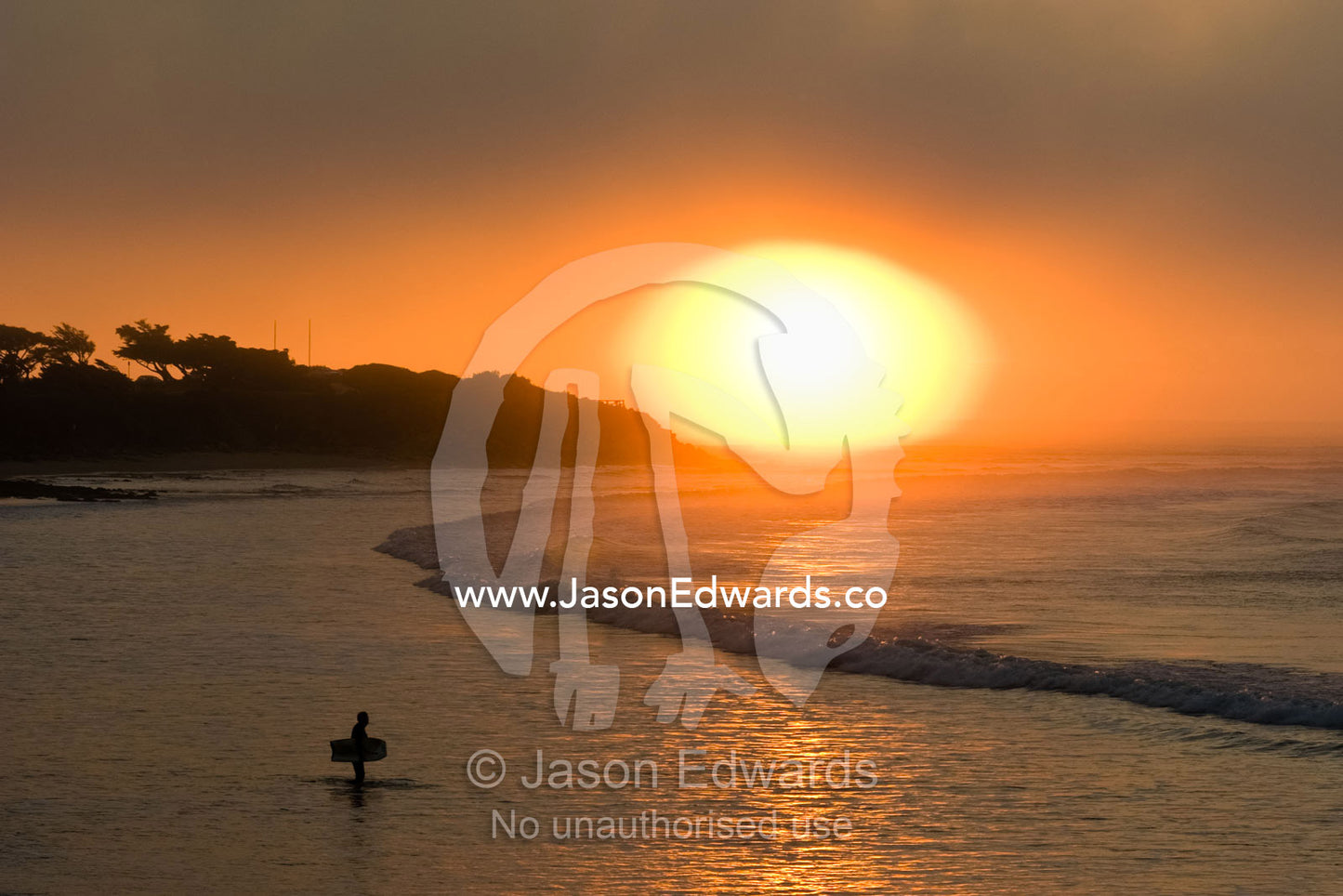 A bodyboarder prepares to go surfing as the sun rises over the ocean. Drainos, Torquay, Surf Coast, Victoria, Australia