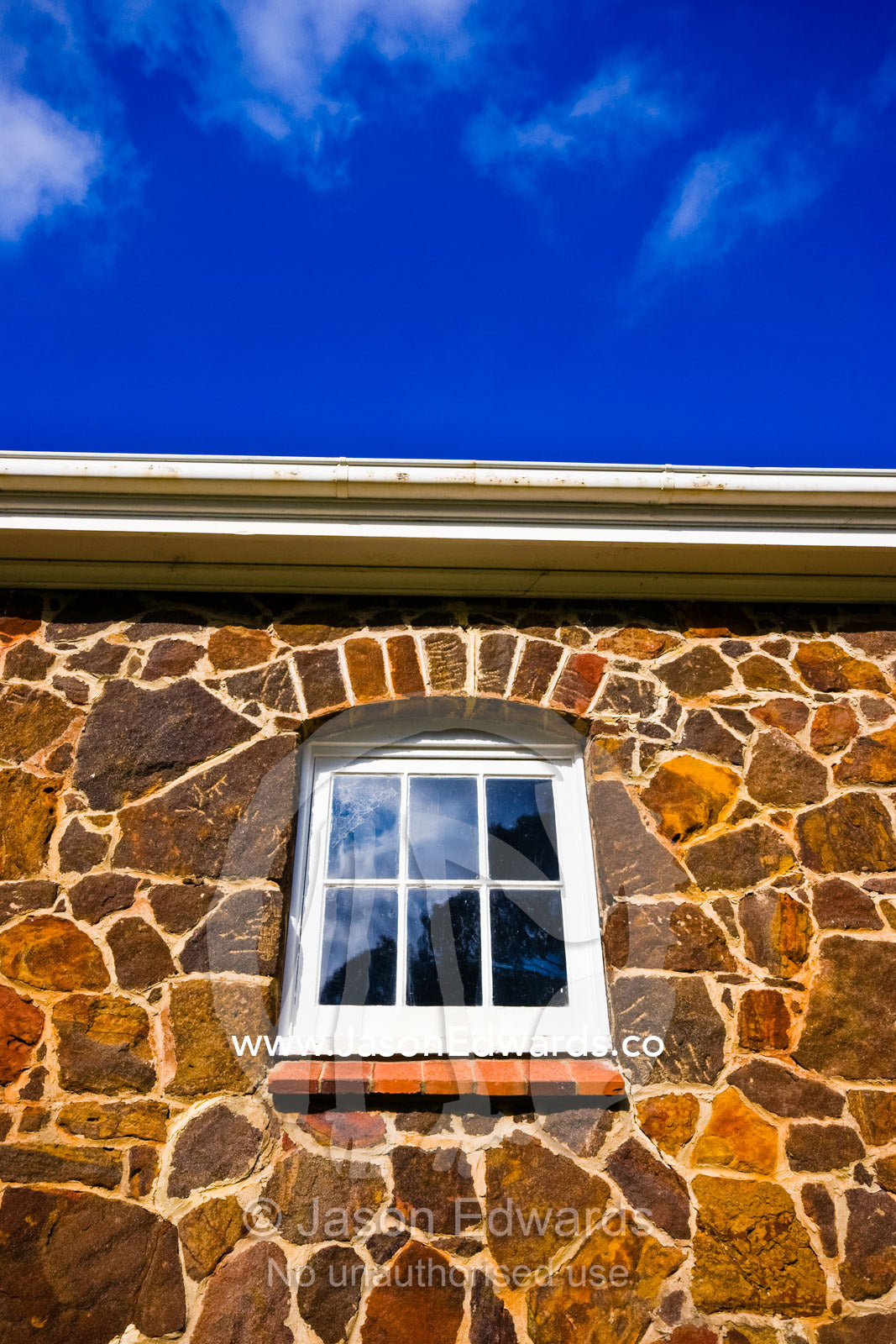 Roughly hewn rocks form a horse stable wall surrounding a window pane. Langwarrin, Victoria, Australia