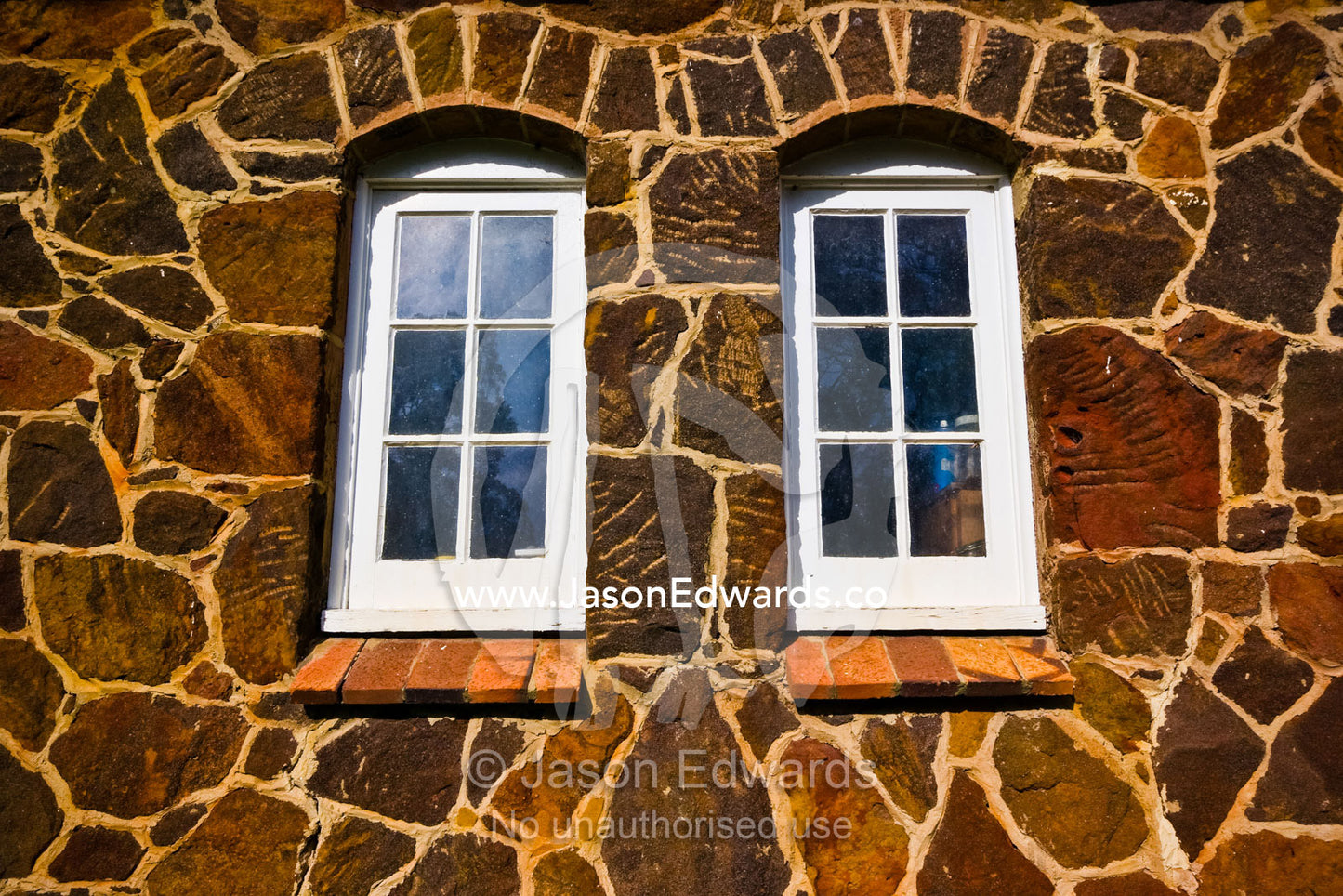 Roughly hewn rocks form a horse stable wall surrounding a window pane. Langwarrin, Victoria, Australia