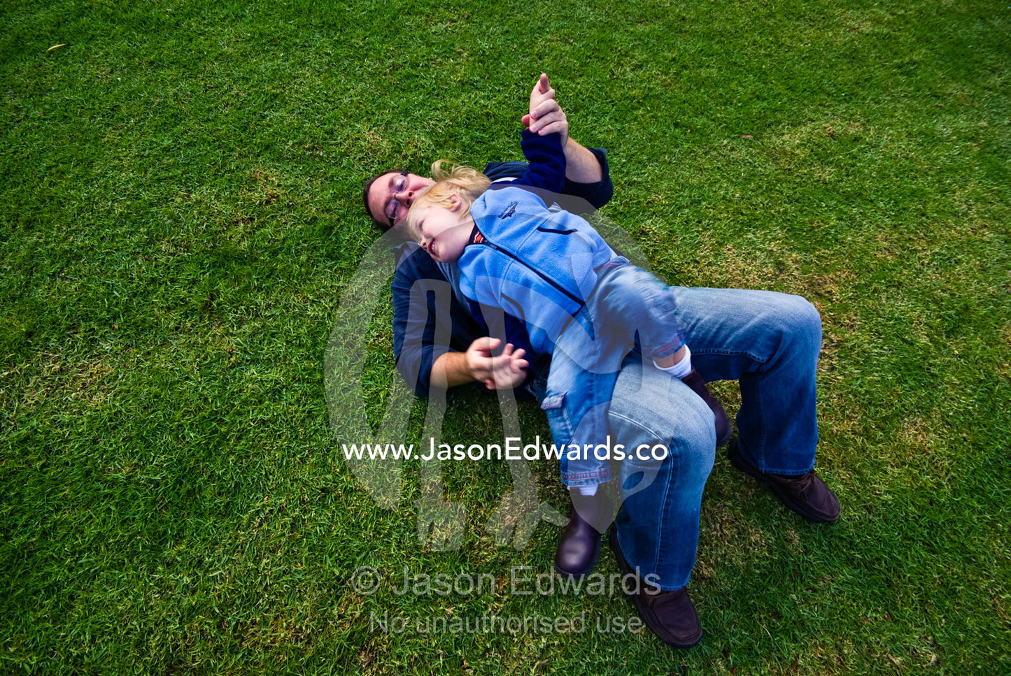 A father and his small son wrestling on a green, manicured lawn. Langwarrin, Victoria, Australia