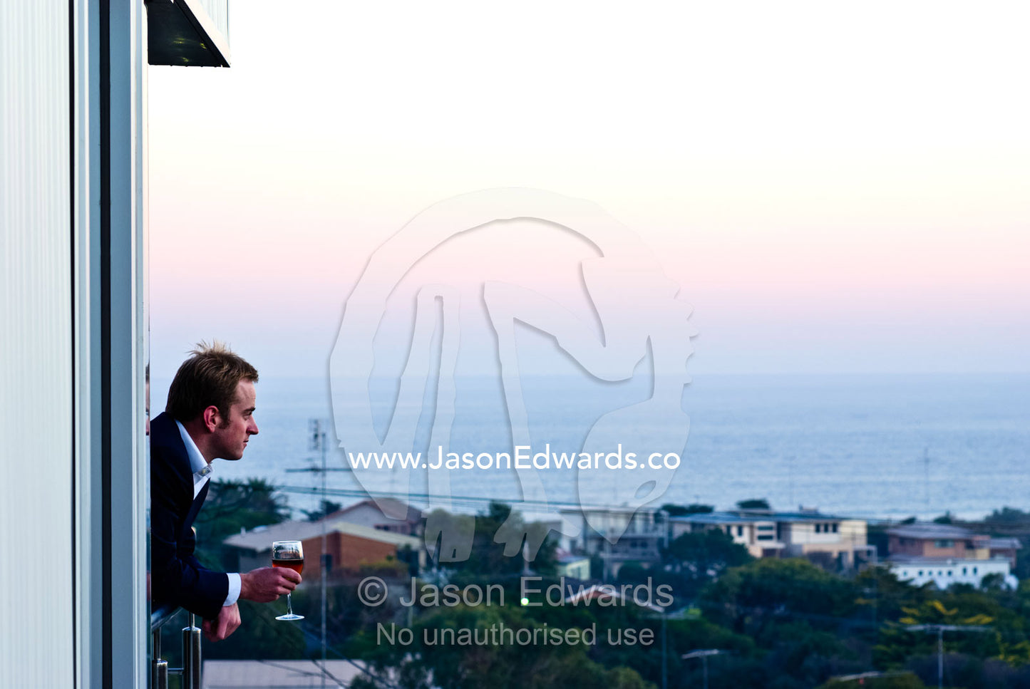 A businessman drinks a glass of wine at sunset from his balcony. Ocean Grove, Victoria, Australia