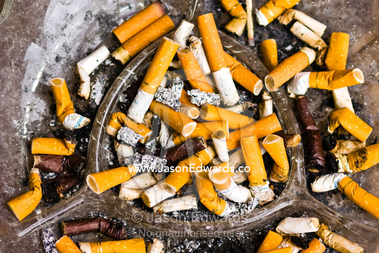 An glass ashtray full of discarded cigarette butts and ash. Collingwood, Victoria, Australia