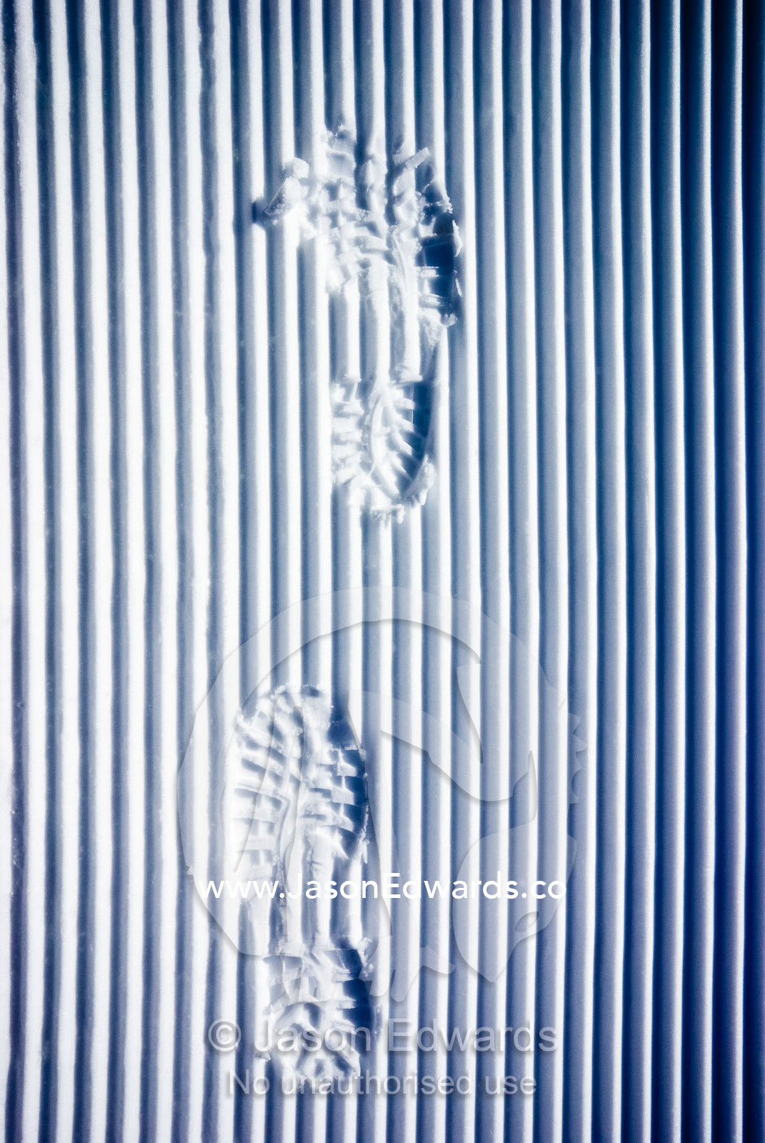 Footprints from hiking boots disrupt linear tracks from a snow plough. Dinner Plain, Victoria, Australia