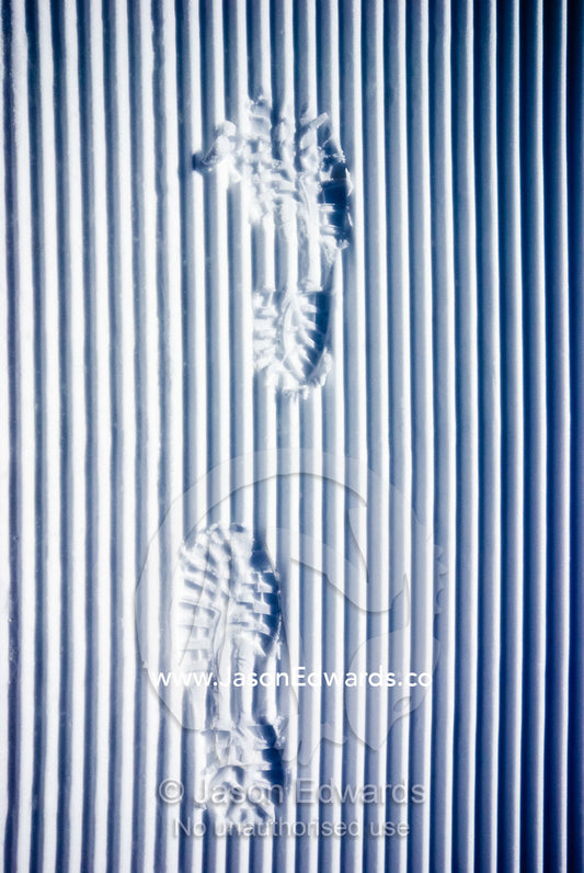 Footprints from hiking boots disrupt linear tracks from a snow plough. Dinner Plain, Victoria, Australia