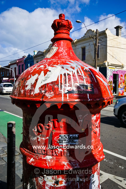An old English mailbox covered in graffiti and illegal advertising. Brunswick Street, Fitzroy, Victoria, Australia